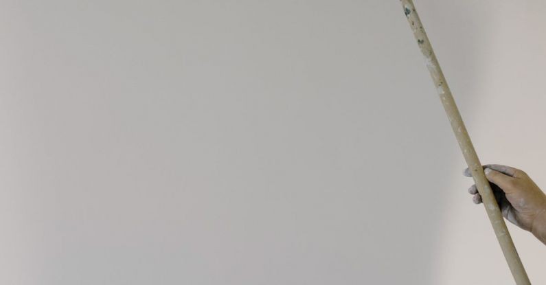 Color Accuracy - Crop anonymous person holding roller with white paint and painting wall in light apartment