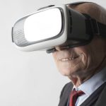Wearables - Smiling elderly gentleman wearing classy suit experiencing virtual reality while using modern headset on white background