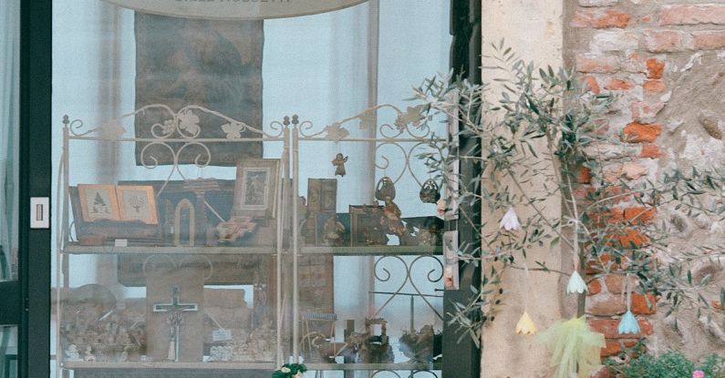 Public Displays - Window of shop of religious articles decorated with potted plants on shabby wall