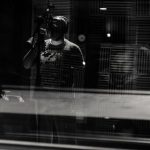 Voice Control - Through glass of black and white anonymous male musician in headphones singing with microphone while recording song in modern studio