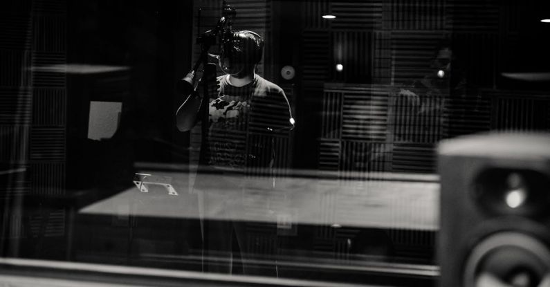 Voice Control - Through glass of black and white anonymous male musician in headphones singing with microphone while recording song in modern studio