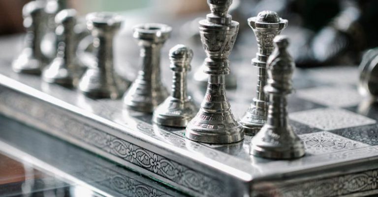 Competitive Play - Classic metal chess board with set figurines designed with carved ornaments and placed on glass table in light room