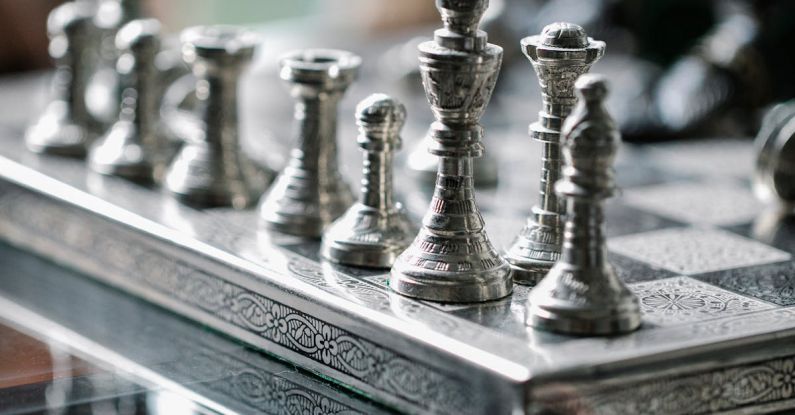 Competitive Play - Classic metal chess board with set figurines designed with carved ornaments and placed on glass table in light room
