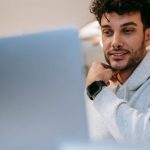 Wearable Screens - Young friendly unshaven male remote worker in wearable tracker against netbook in light house room
