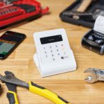 Screen Maintenance - Red and black toolboxes next to smartphone and modern cash registers composing with pliers and wrenches on beige wooden table in bright room